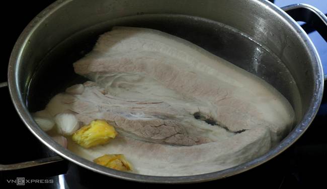 Một miếng thịt heo được cho vào nồi nước, vài lát hành, chút muối, rồi chờ nước sôi.